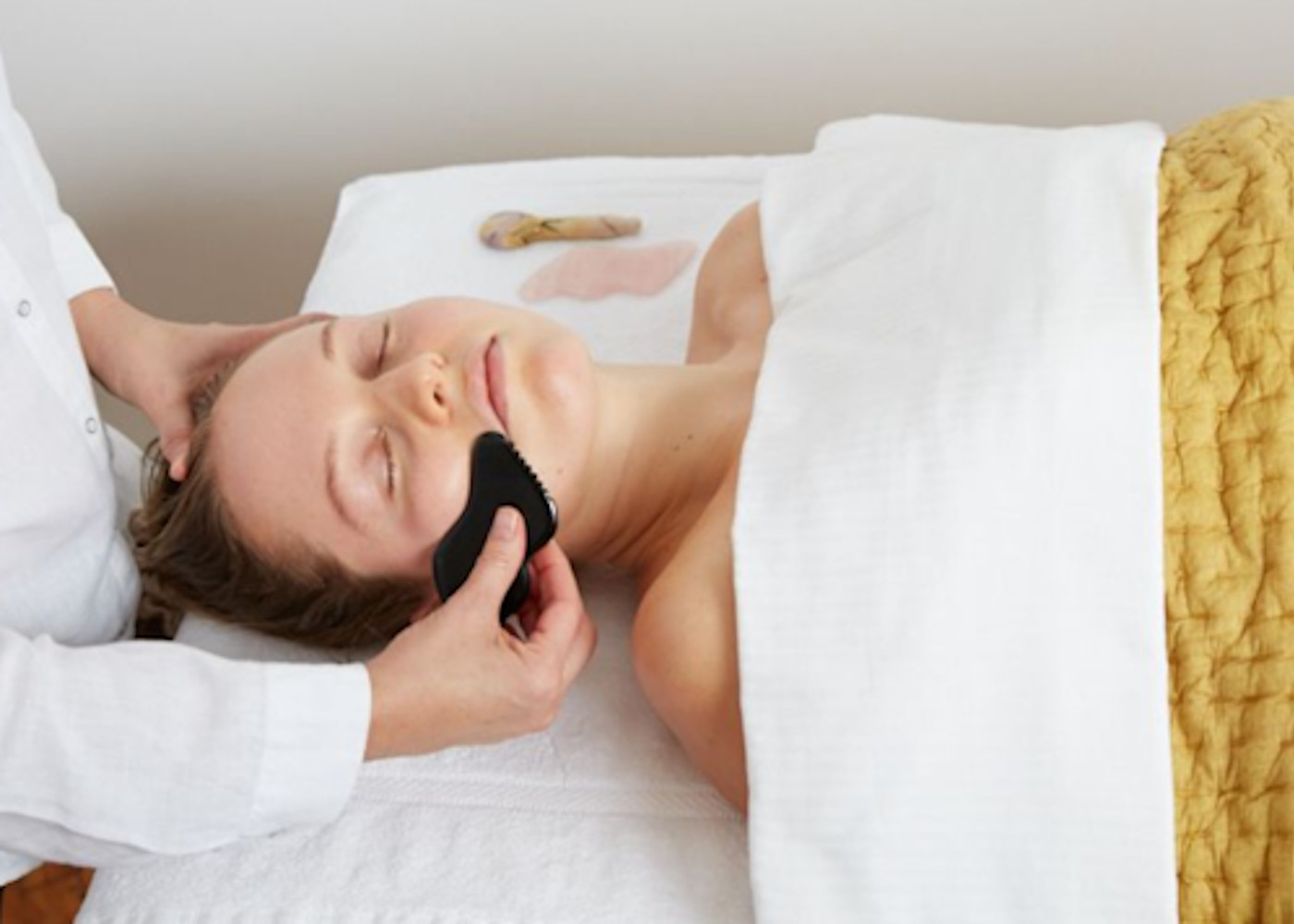 Women laying down on a couch with her eyes closed enjoying a Gua Sha Facial Fusion treatment